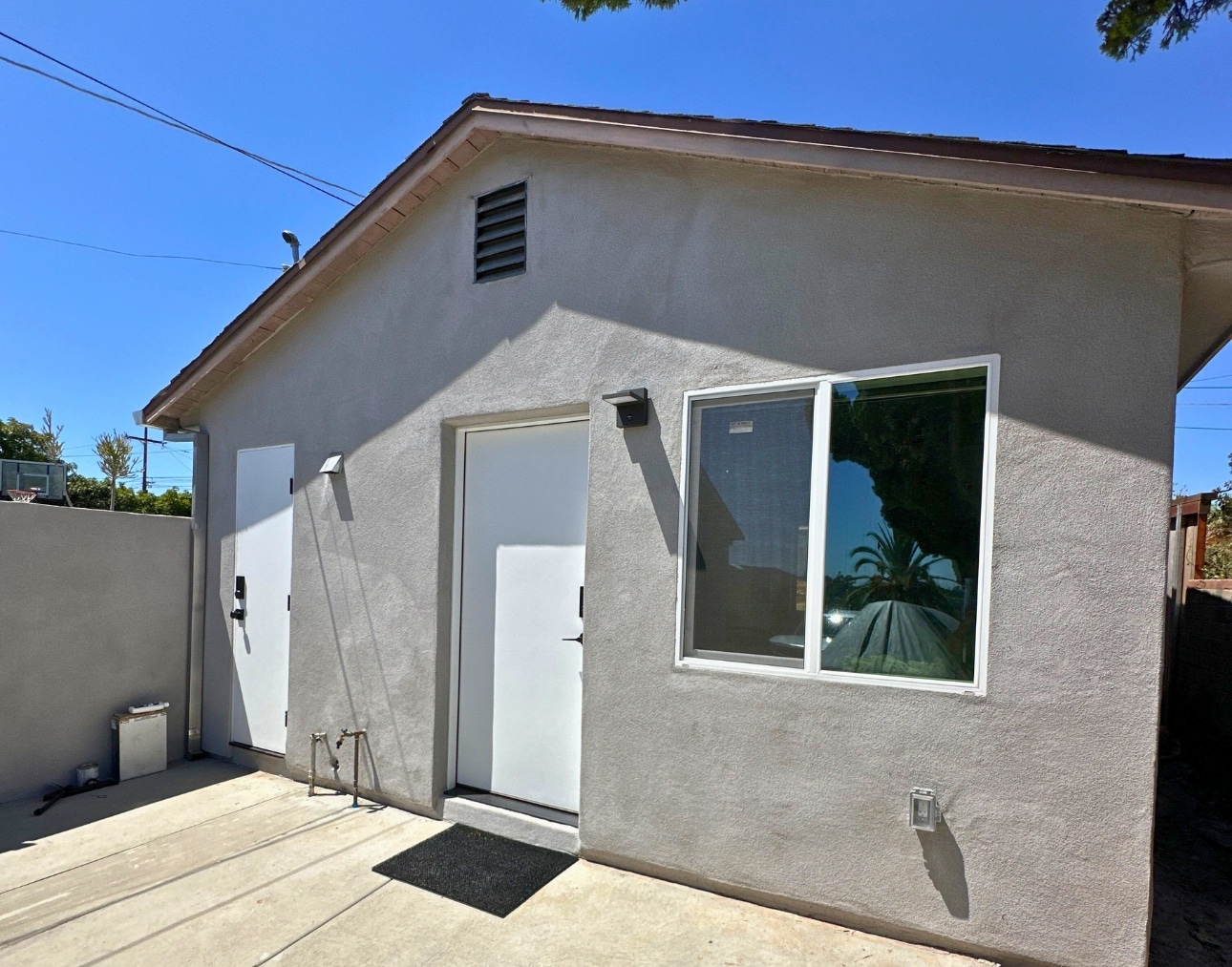 A detached ADU with a smooth stucco exterior, white doors, and a large window, emphasizing the benefits of ADUs as private, functional living spaces that enhance property value.