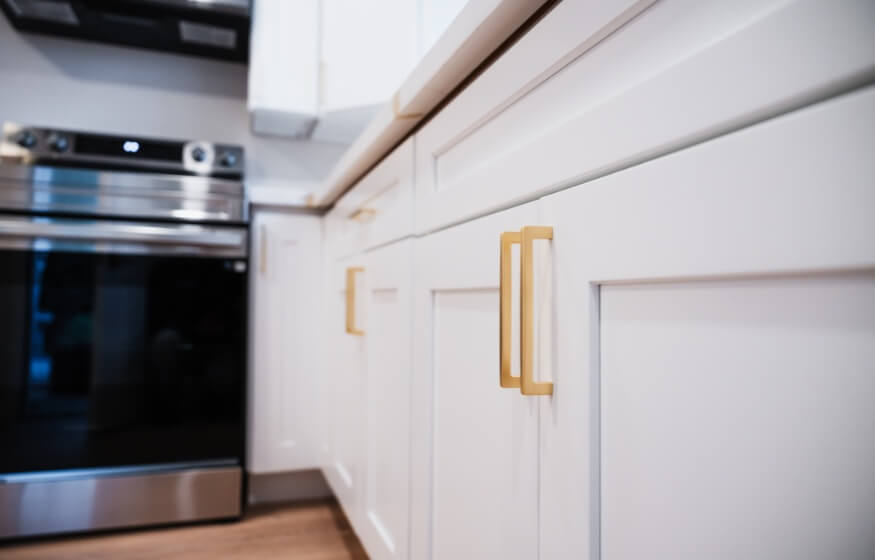 Modern kitchen interior of a newly built ADU in Santee, featuring white cabinetry with gold hardware and stainless steel appliances.