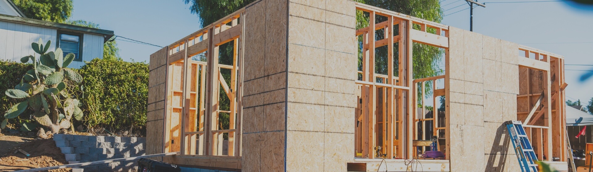 ADU under construction in Santee, with exterior walls framed and plywood sheathing installed, surrounded by lush greenery.