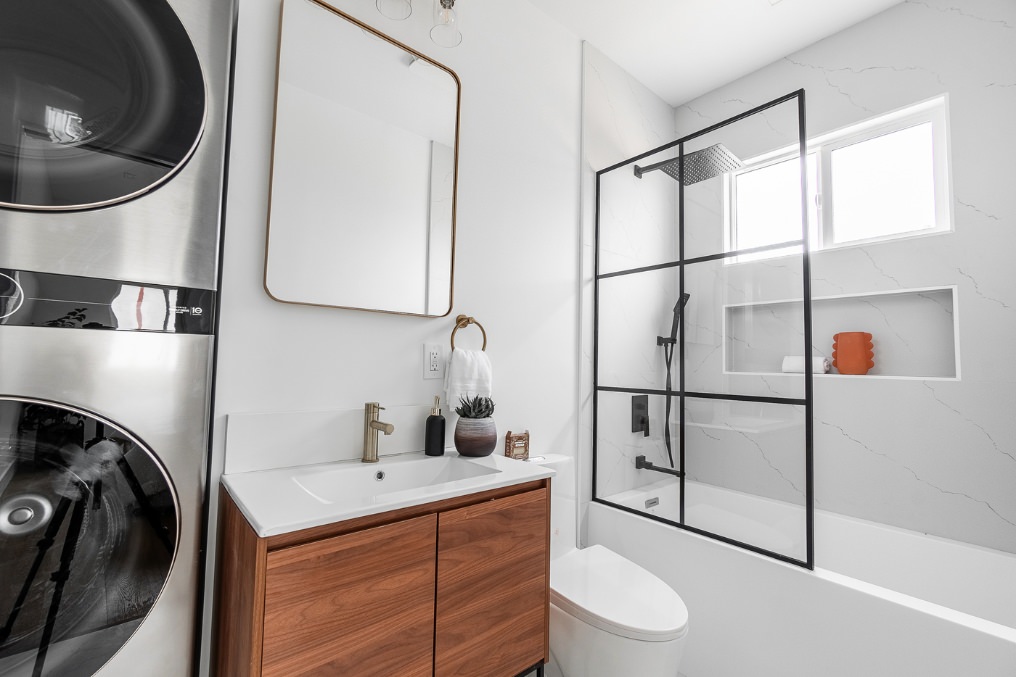 Compact bathroom with walnut vanity, modern fixtures, and stacked washer-dryer in Pacific Beach detached ADU.