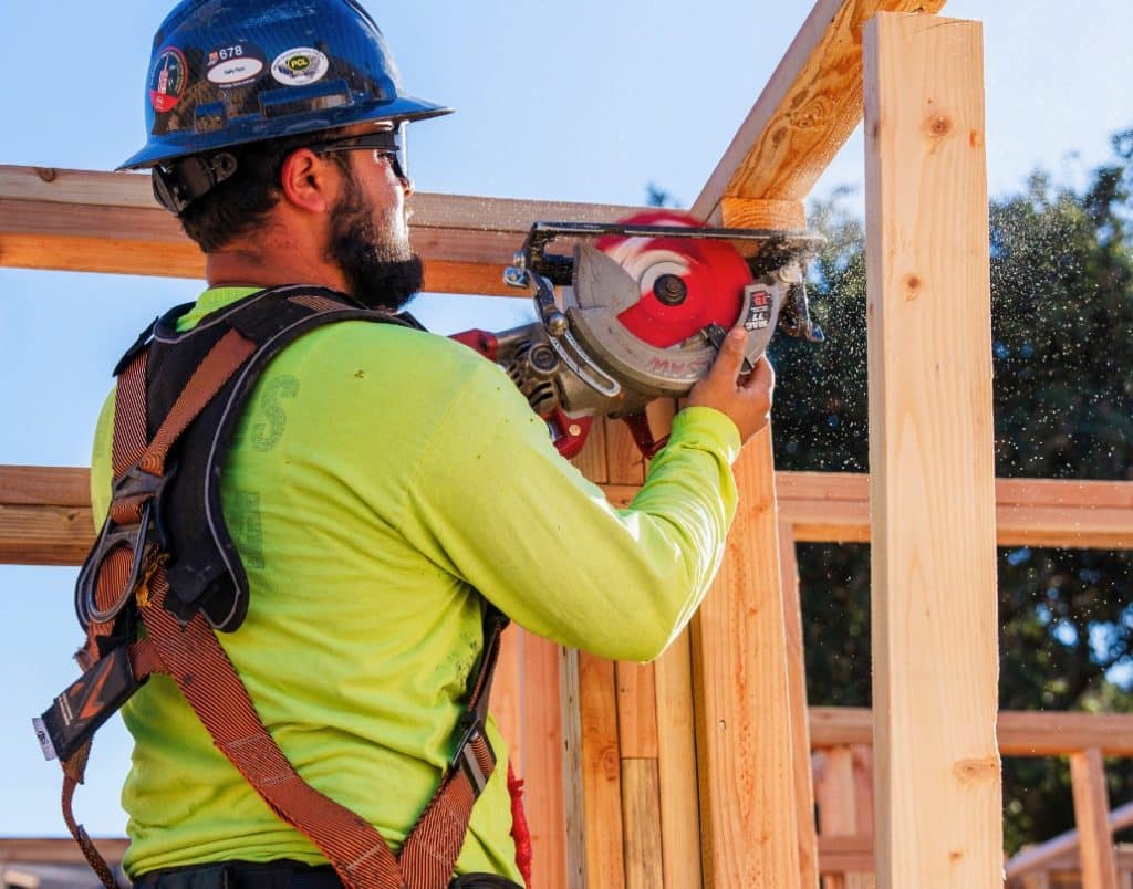 A construction worker in safety gear actively cutting wood for framing an ADU.