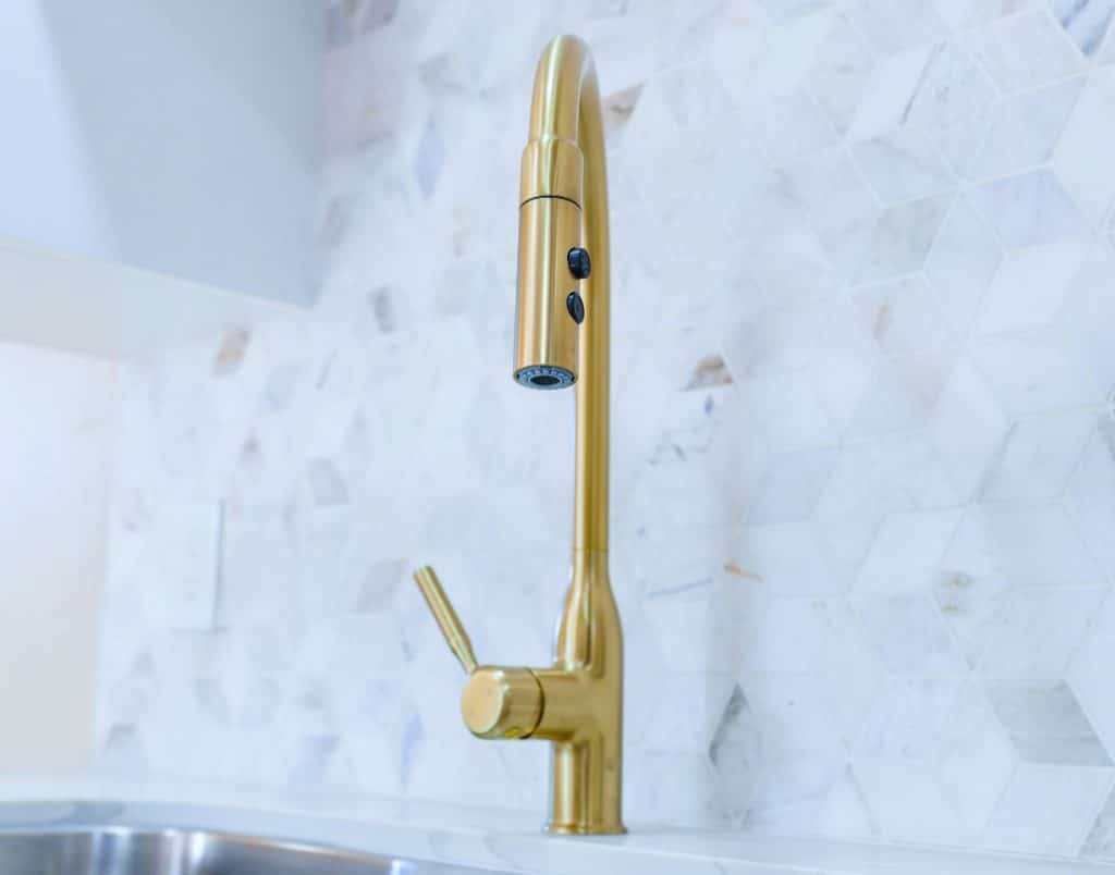 A sleek, gold kitchen faucet with hexagonal backsplash tiles in a modern ADU kitchen.