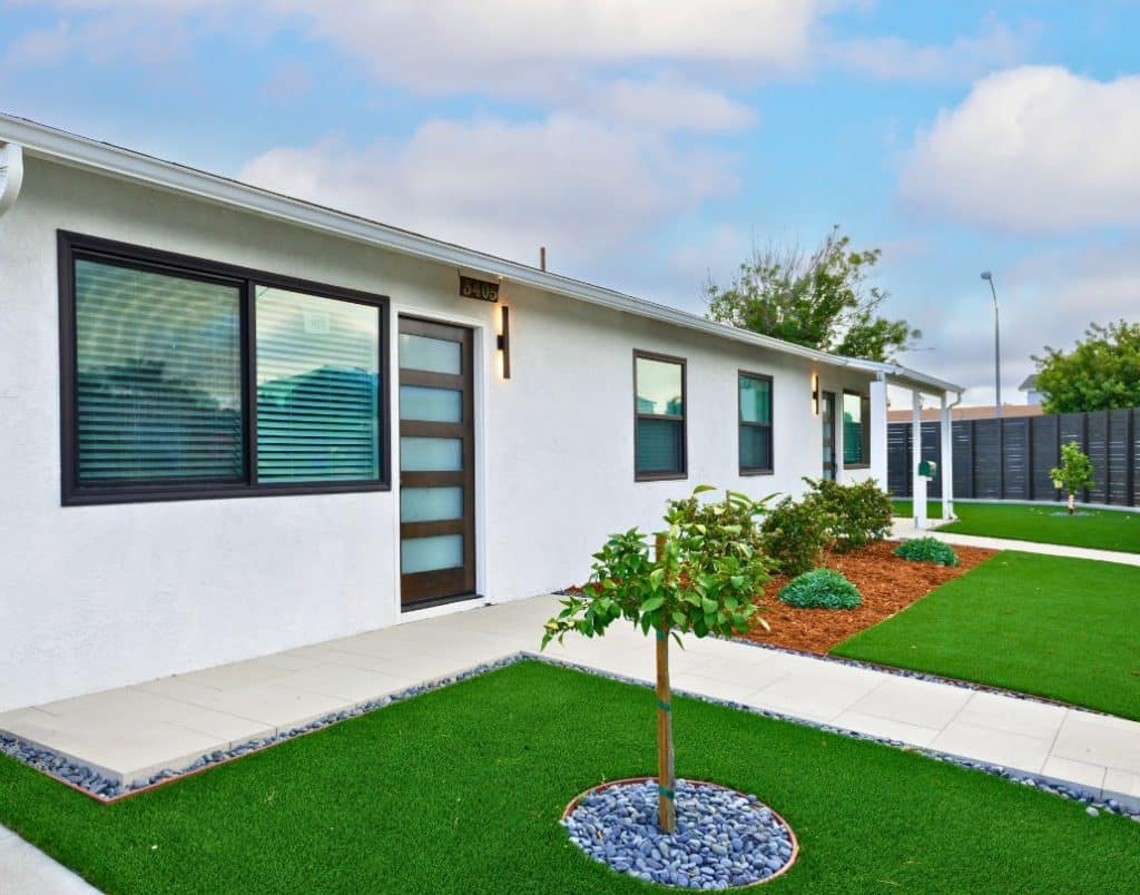 A beautifully landscaped ADU exterior with artificial grass, modern siding, and young trees planted along the walkway.