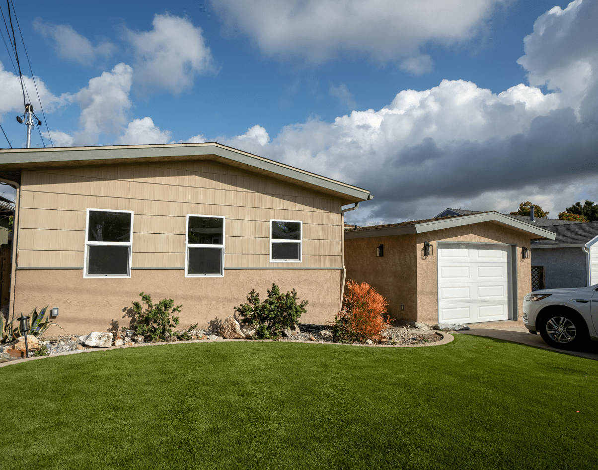 Exterior view of a modern ADU garage conversion, featuring a beige stucco exterior and lush artificial grass lawn under a blue sky. This ADU project aligns with ab1033 regulations, offering a stylish and functional living space upgrade.