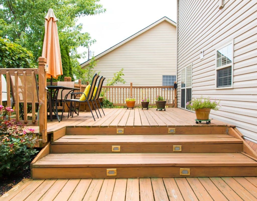 A wooden deck with integrated steps featuring built-in lighting, surrounded by potted plants and outdoor furniture.