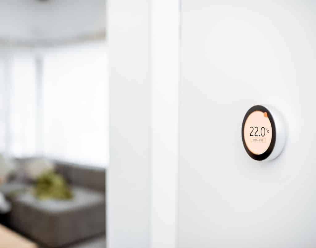 Smart thermostat mounted on a wall displaying home temperature and energy usage settings.