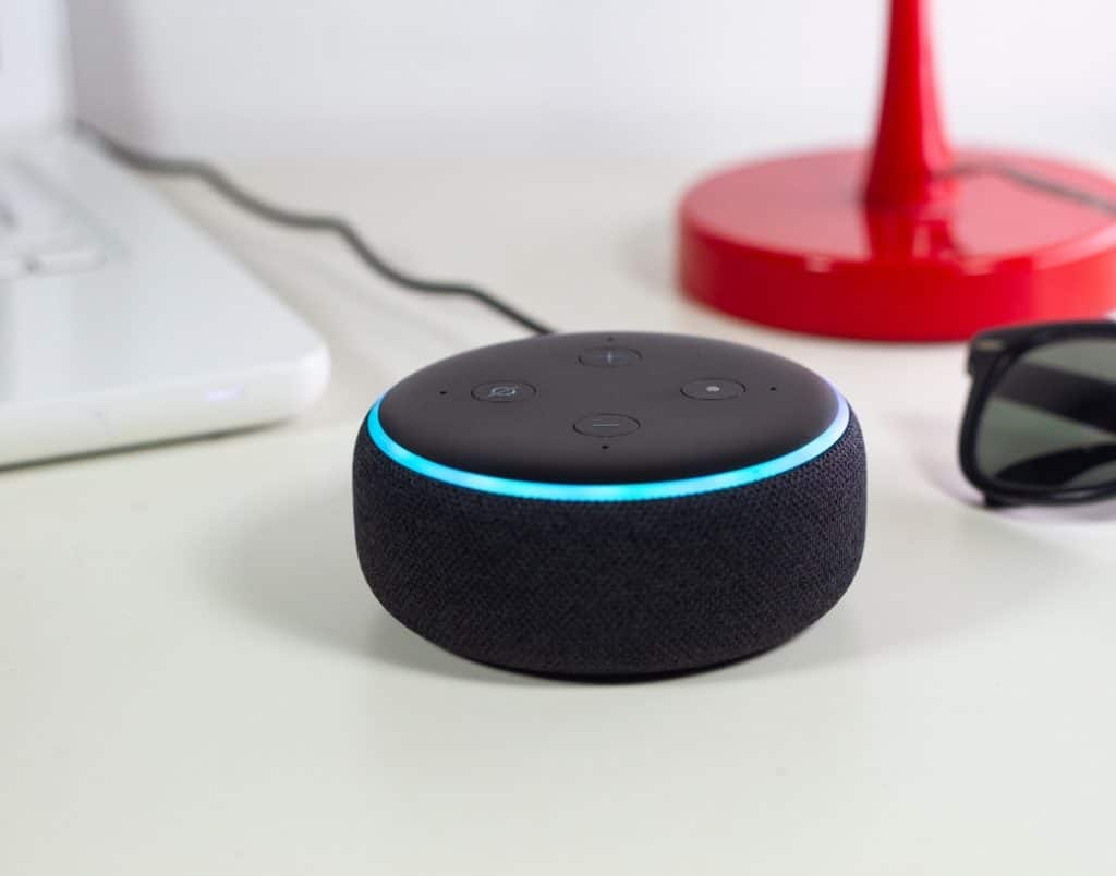 Voice-activated smart assistant device on a desk, paired with modern tech for home automation.