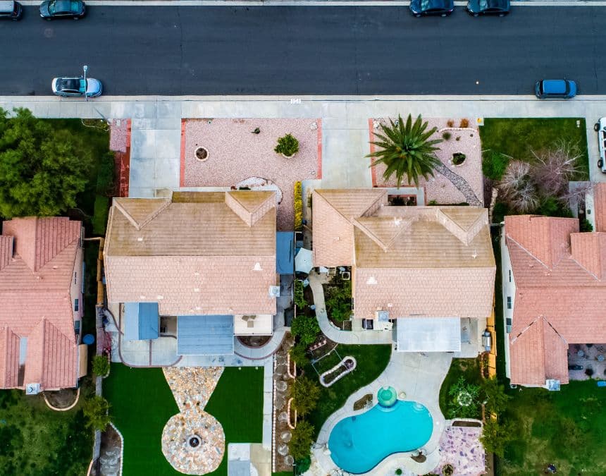 Aerial view of suburban homes with landscaped backyards, including a pool and seating areas. Highlights the potential placement and spatial requirements for ADUs versus pool houses, illustrating how ADUs can integrate into residential properties while serving distinct purposes compared to recreational pool houses.