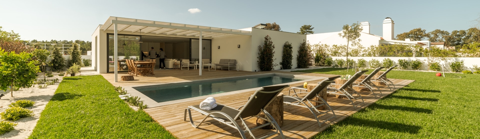 "Luxurious backyard setup featuring a modern pool house with shaded seating, a pool, and a sun deck with loungers. This design exemplifies the versatility of pool houses and ADUs, offering a stylish outdoor living area that blends relaxation and functionality, perfect for entertainment or guest accommodations.