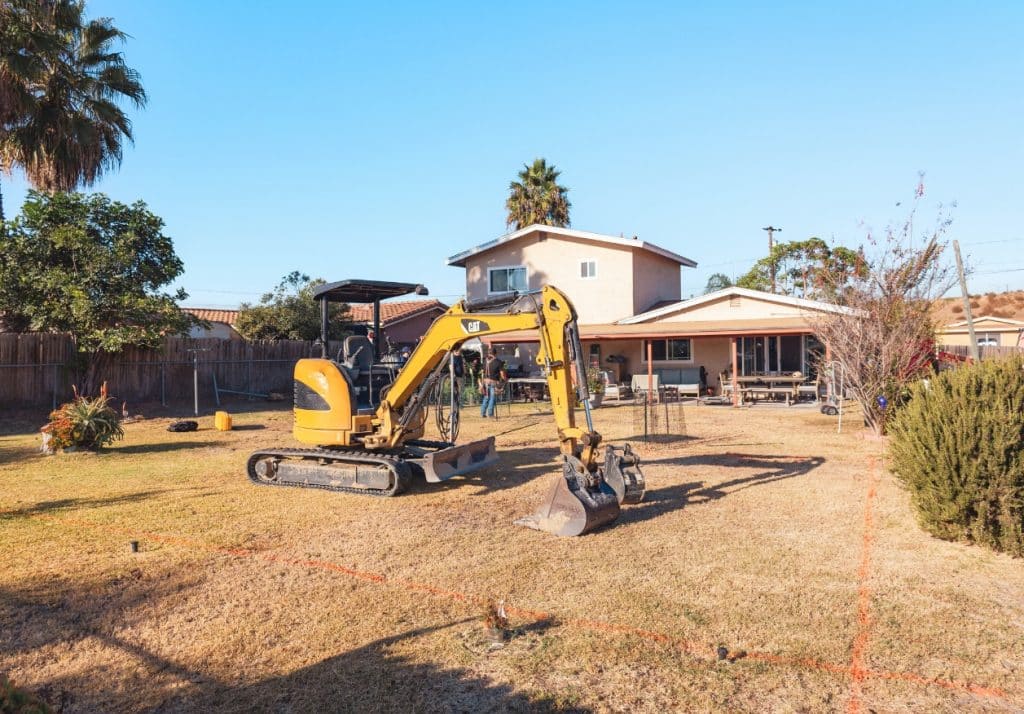 Excavator on-site at a residential property highlighting poor construction choices and site preparation challenges for ADU builds.