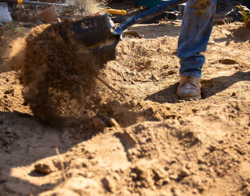 A construction worker preparing the ground for an ADU foundation during the excavation phase.