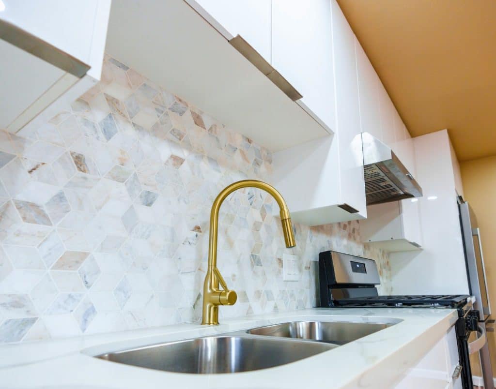 Modern ADU kitchen with a sleek gold faucet, stainless steel sink, and premium backsplash tiles showcasing quality materials.