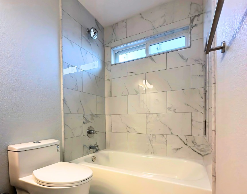 Modern ADU bathroom with bathtub, toilet, and tiled shower, illustrating how plumbing fixture choices impact ADU costs.