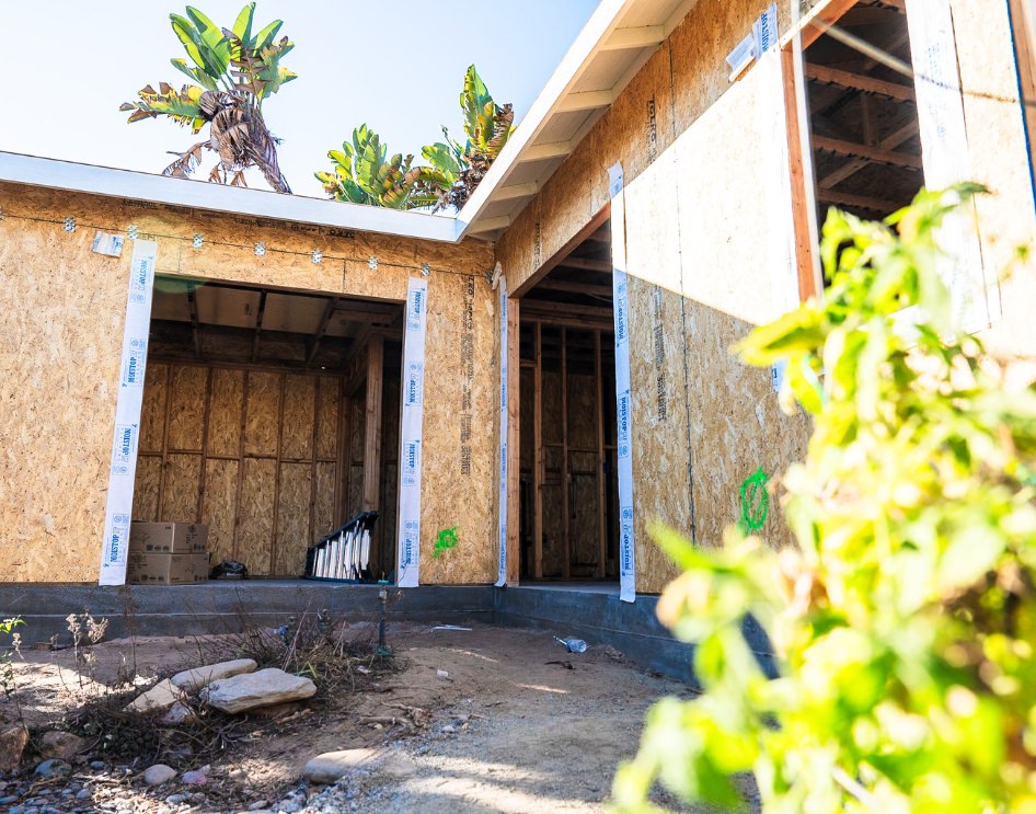 A construction site with framed ADU walls in progress, surrounded by landscaping.