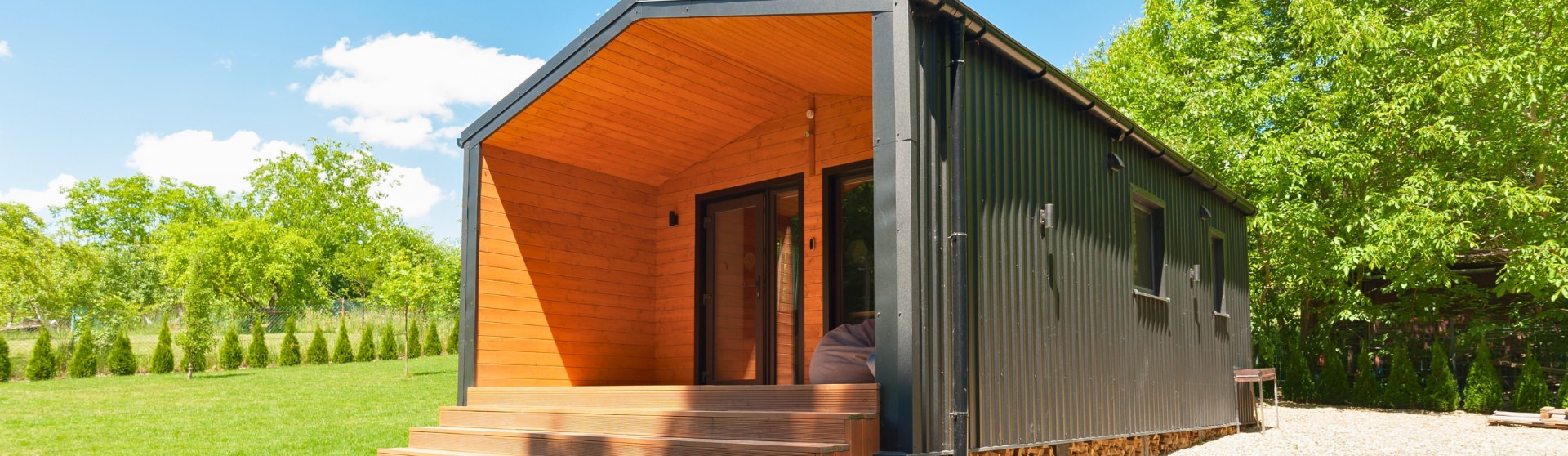 Modern manufactured ADU with black metal siding and wood accents in a green backyard.