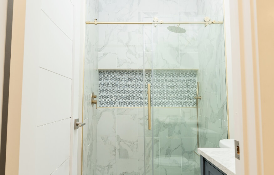 Modern tiled shower with glass doors and gold fixtures in a 950 sq ft ADU bathroom, featured in the FAQ section.