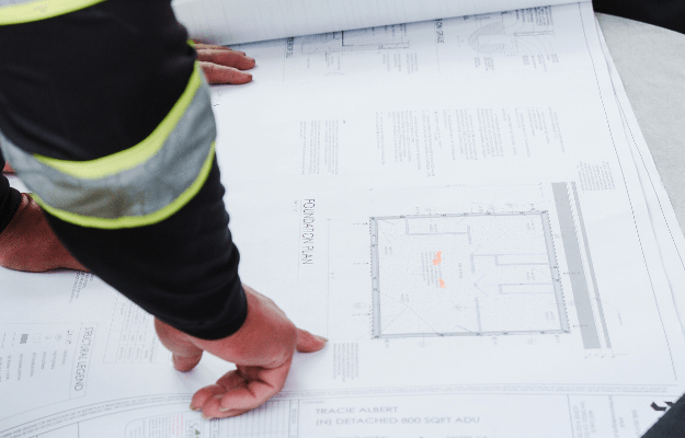Construction worker reviewing architectural plans inside a wood-framed structure during the design phase – Turn vision into plans