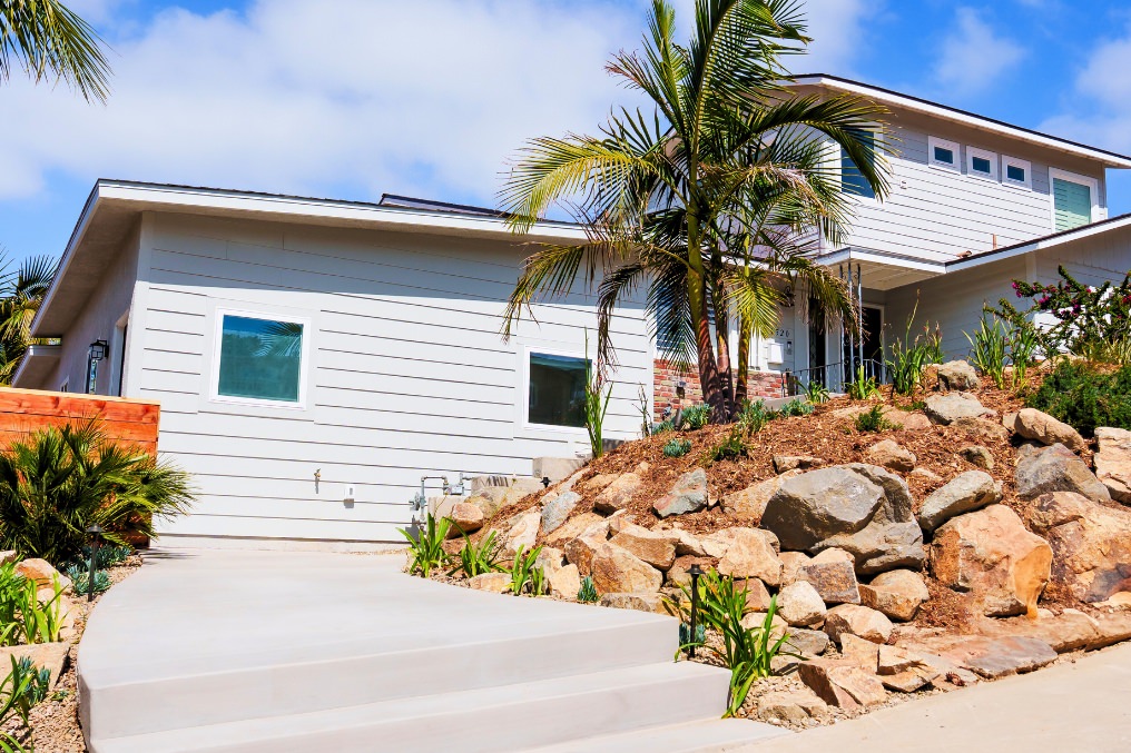 Front exterior of stylish attached ADU featuring modern siding, lush landscaping, and coastal aesthetic.