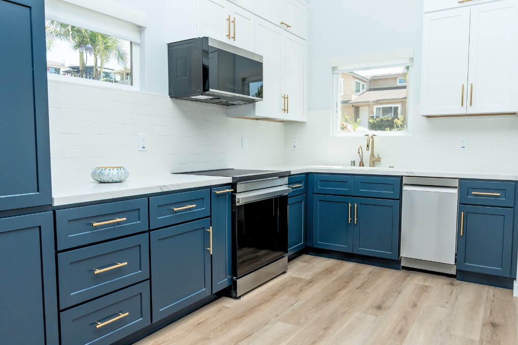 Modern coastal kitchen featuring navy blue cabinets, white countertops, gold hardware, and stainless appliances.