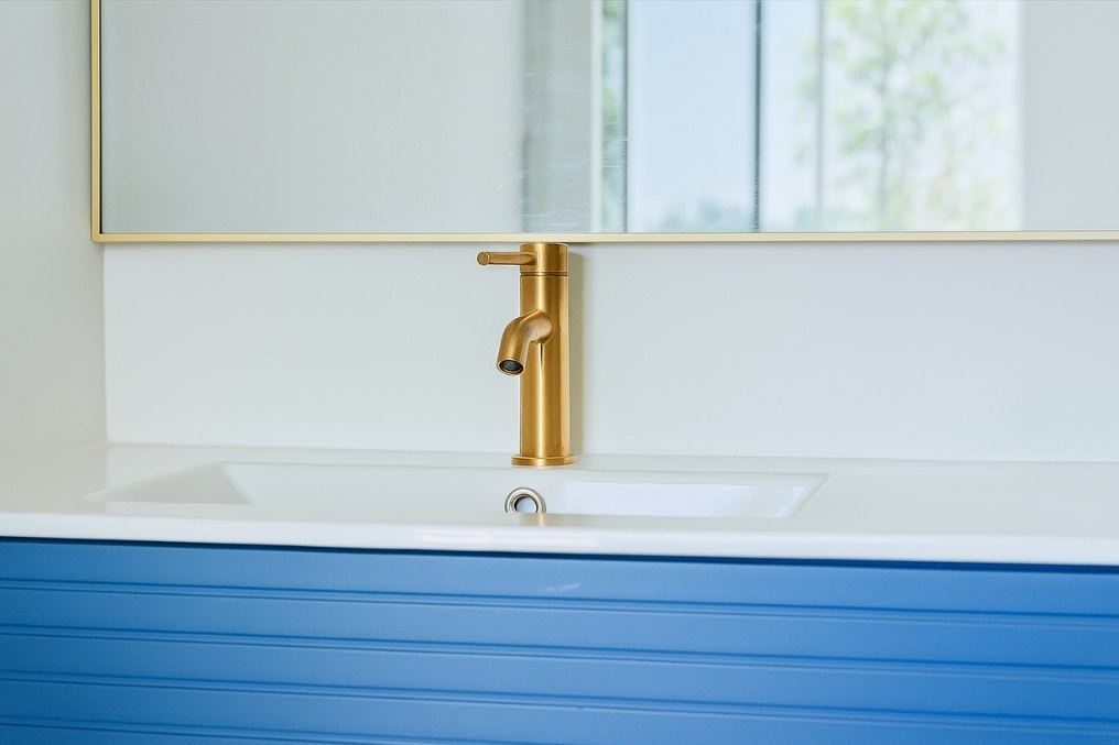 Close-up view of sleek blue vanity with white countertop and elegant gold faucet in ADU bathroom