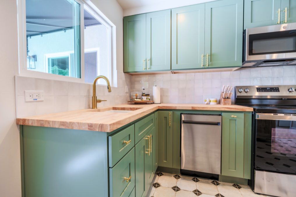 Modern boho kitchen with green cabinetry, butcher-block countertops, and brass fixtures