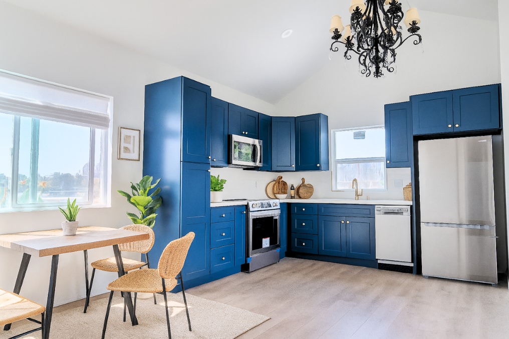 Open-concept kitchen and dining area with bold blue cabinets, stainless steel appliances, and modern chandelier
