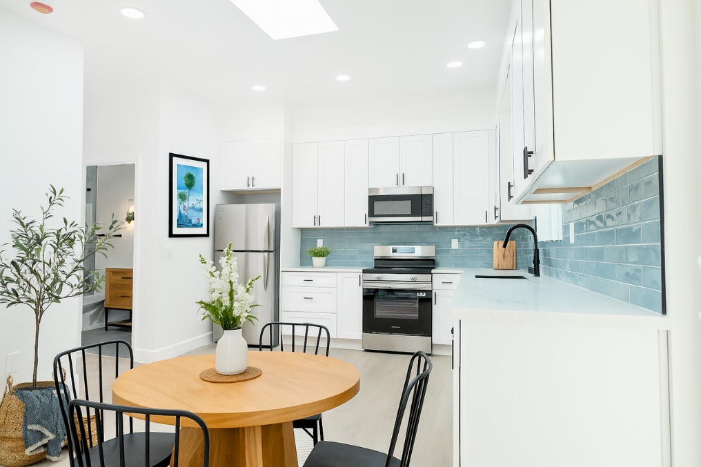 Open kitchen with white cabinets, blue backsplash, and modern dining area in garage conversion ADU