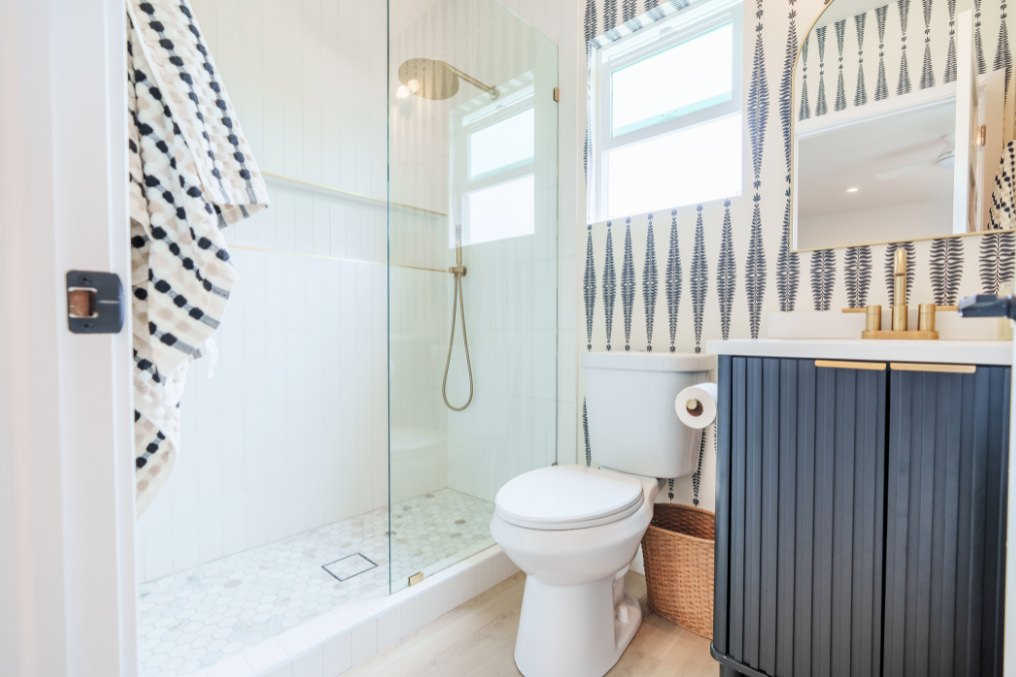 Elegant boho bathroom showcasing minimalist glass shower enclosure, gold fixtures, and patterned wallpaper