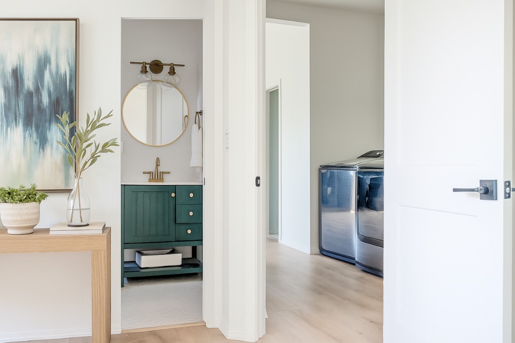 Elegant coastal-themed bathroom featuring teal vanity, gold hardware, and decorative mirror