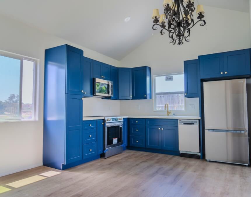 Completed ADU kitchen featuring royal blue cabinets, brass fixtures, and a black chandelier