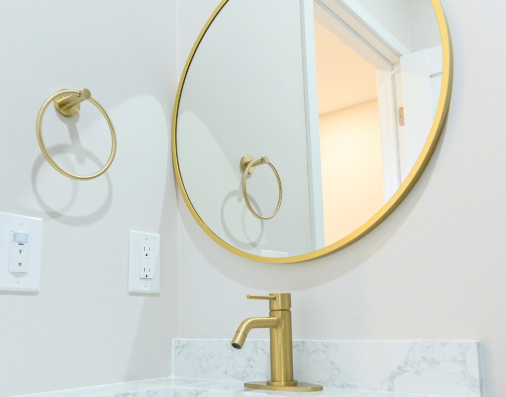 Del Mar Rental Oasis 4 bathroom design featuring brass fixtures and round mirror.