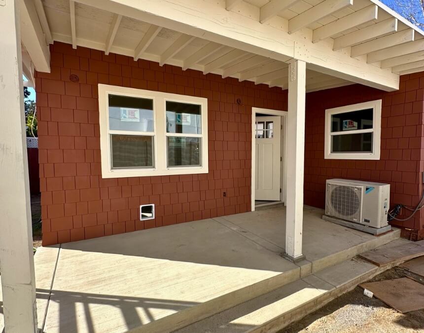 Rear view of a small red-shingled guest house with mini-split HVAC system and side porch