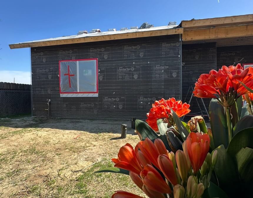 Exterior of an ADU under stucco wrap construction with flowers in the foreground and a red-taped window.