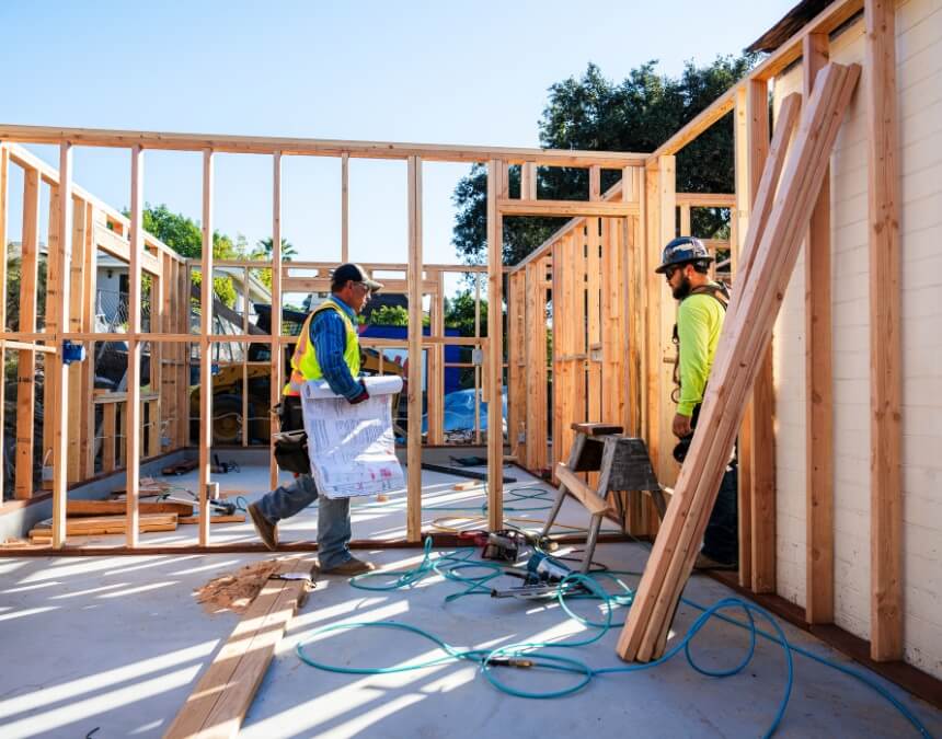 Two builders reviewing floor plans on-site during framing.