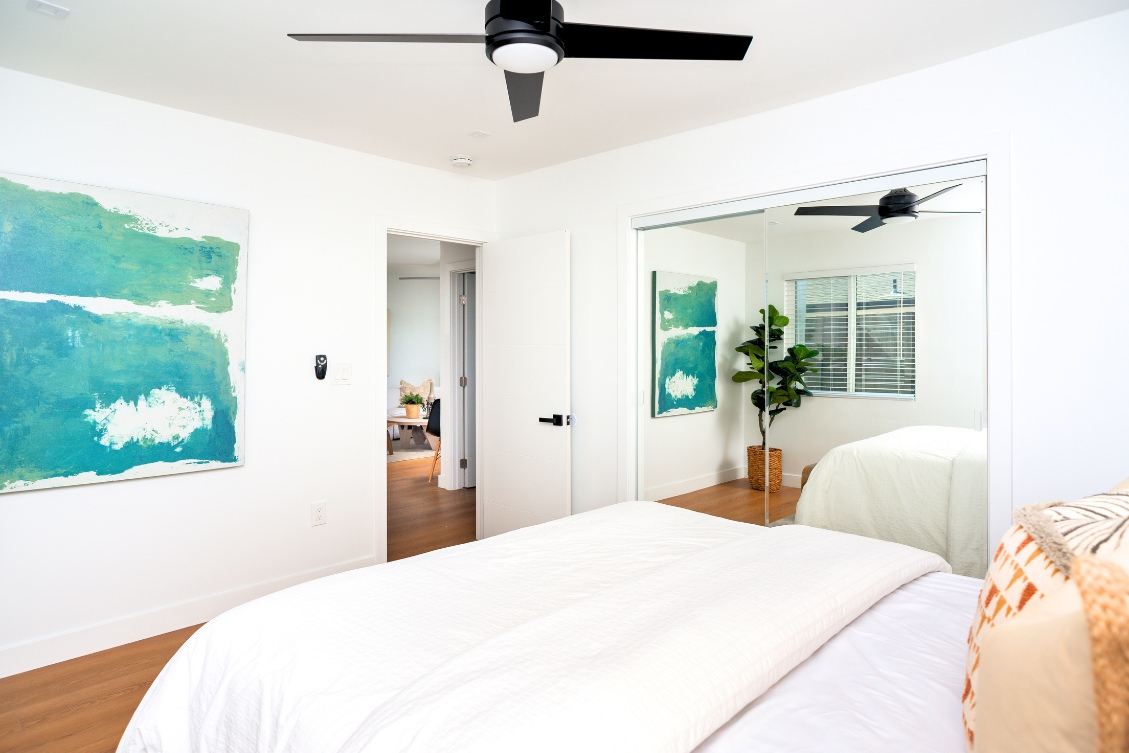 Bright ADU bedroom with potted plant décor, round wall mirror, and neutral bedding