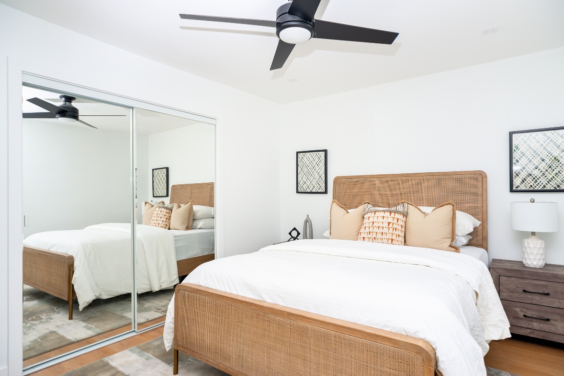 Minimalist ADU bedroom with bold teal wall art, mirrored closet, and ceiling fan