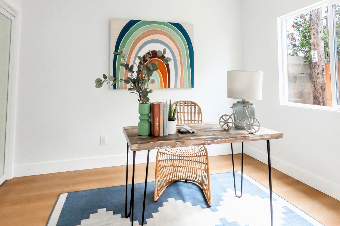 ADU flex space staged as a bedroom or office with rainbow wall art, desk, and woven chair