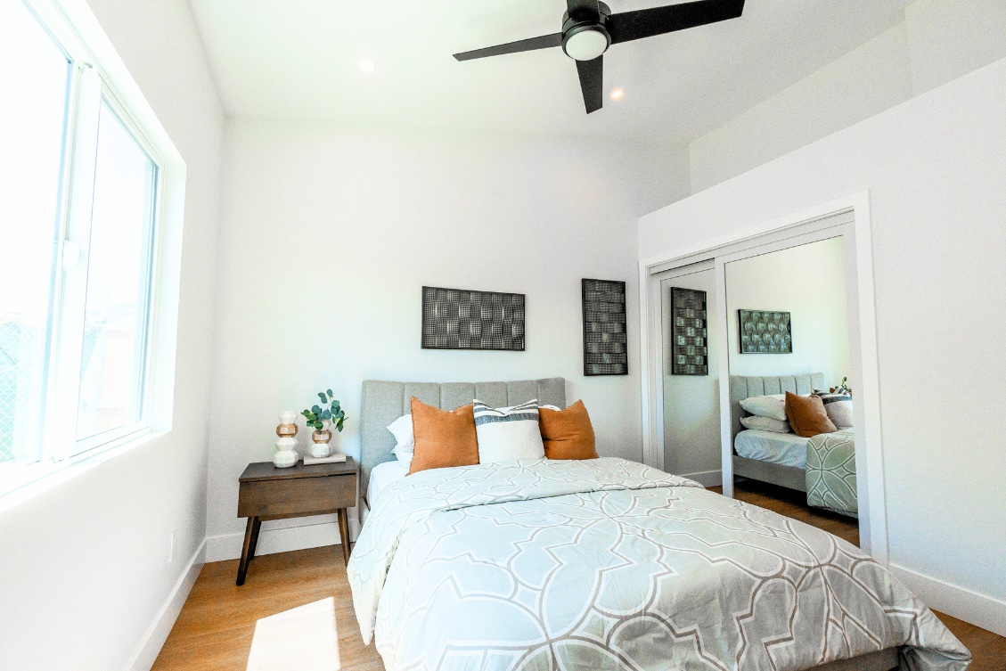 Bright ADU bedroom with ceiling fan, gray headboard, and accent pillows