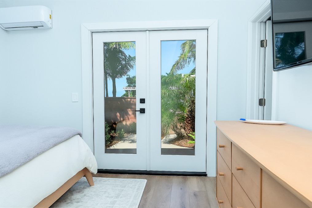French doors from master bedroom of coastal attached ADU showcasing outdoor greenery views.
