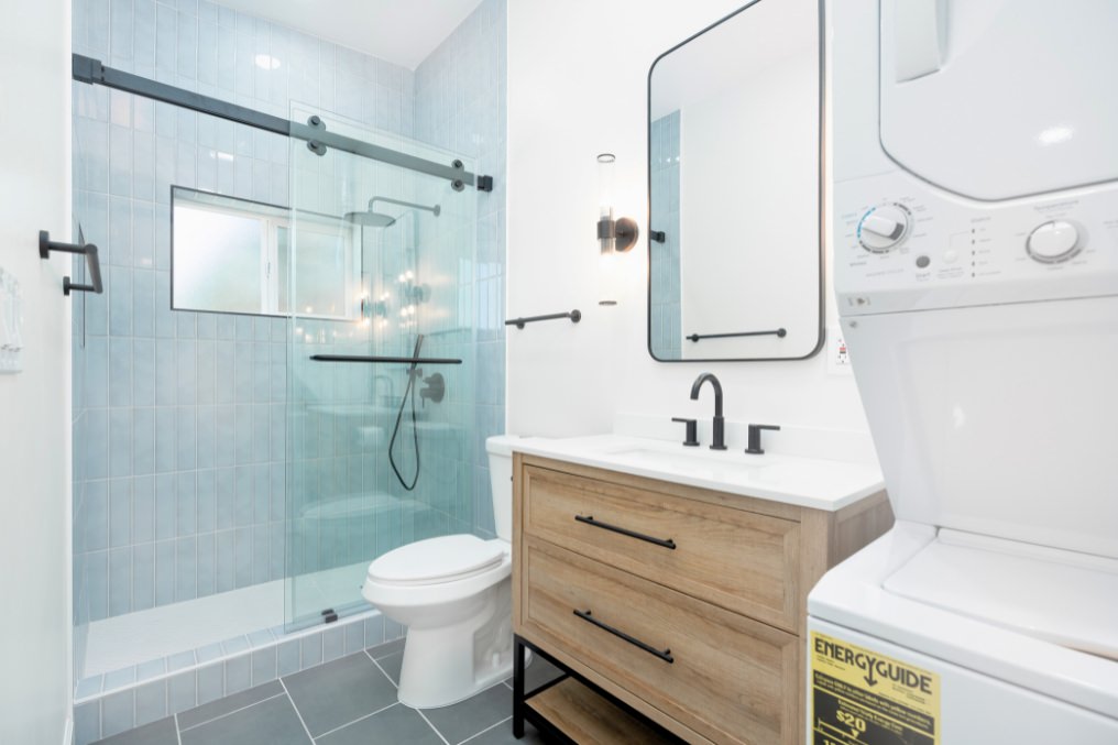 Contemporary bathroom with blue-tiled shower, modern fixtures, and laundry space in garage conversion ADU
