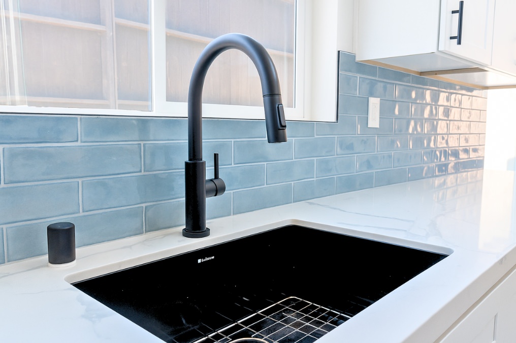 Close-up of stylish black faucet, white countertop, and blue backsplash in ADU kitchen