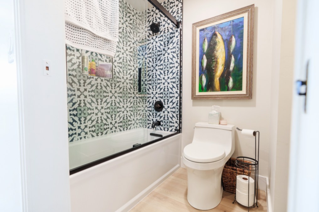 Stylish bohemian bathroom featuring bold geometric tiles, glass-enclosed bathtub, and artistic wall decor