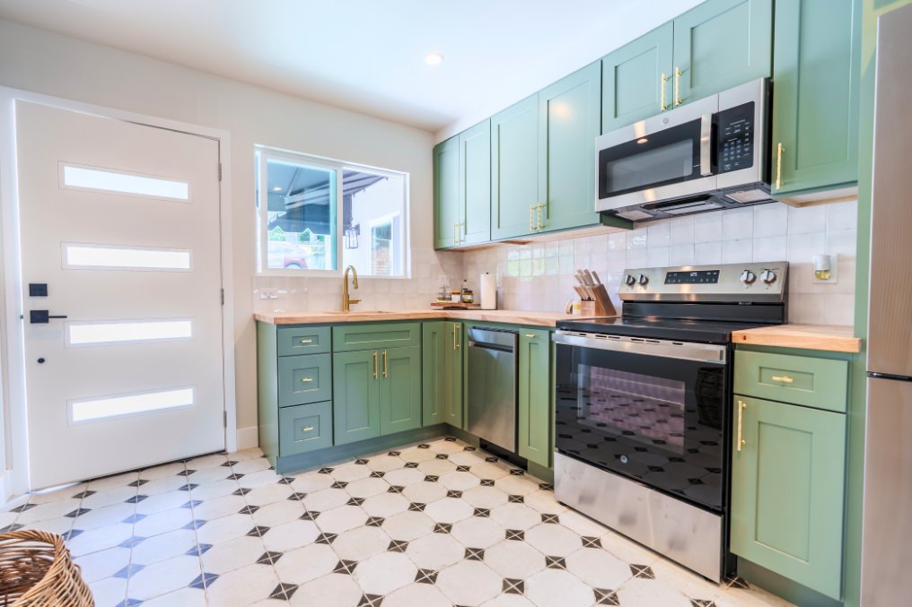 Bright and airy boho-chic kitchen featuring green cabinets, stainless steel appliances, and patterned flooring