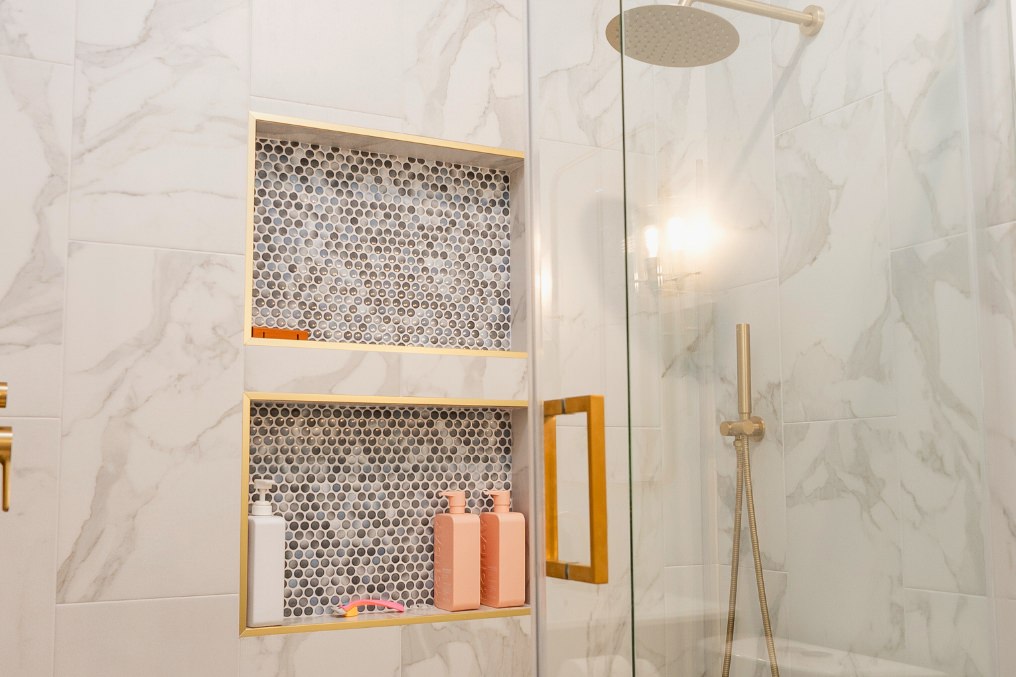 Close-up of a modern shower featuring marble tile, hexagonal mosaic niches, and gold fixtures in an attached ADU bathroom.