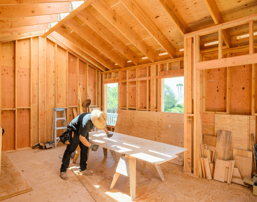 Contractor working inside an ADU during daylight, surrounded by natural wood framing and open windows that allow cross-ventilation.