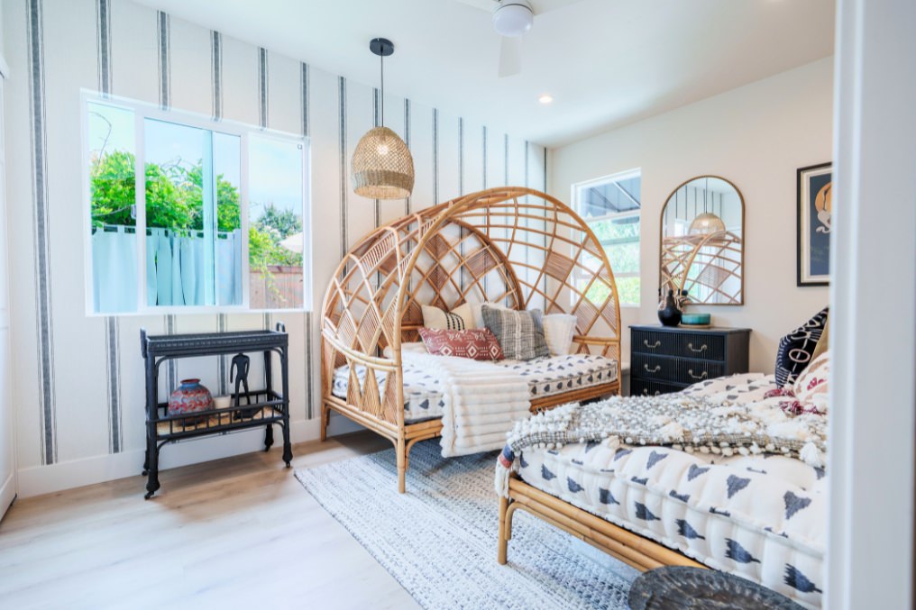 Bright and inviting guest room with boho accents, patterned wallpaper, and rattan furniture in detached ADU