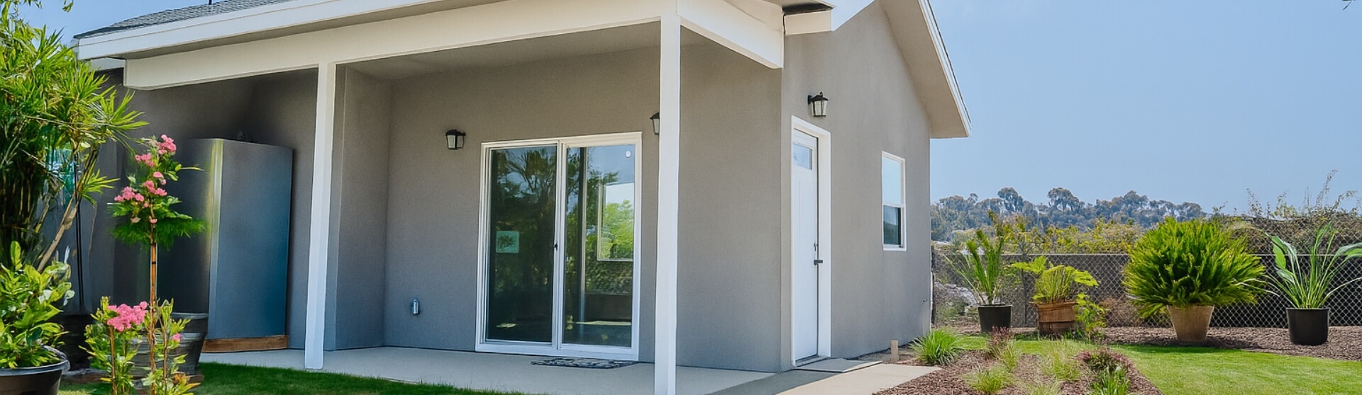 Exterior view of a detached ADU in California with sliding glass door, white trim, and landscaped yard