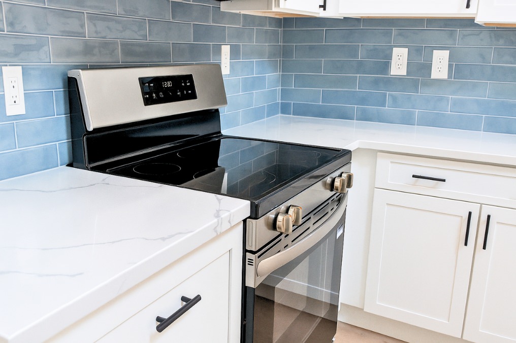 Sleek black and stainless range with white quartz counters and blue tile backsplash in garage ADU