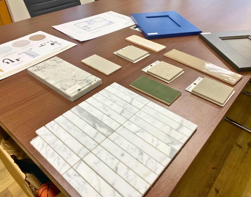 Construction materials and interior finish samples laid out on a design boardroom table, next to blueprints and cabinet fronts.