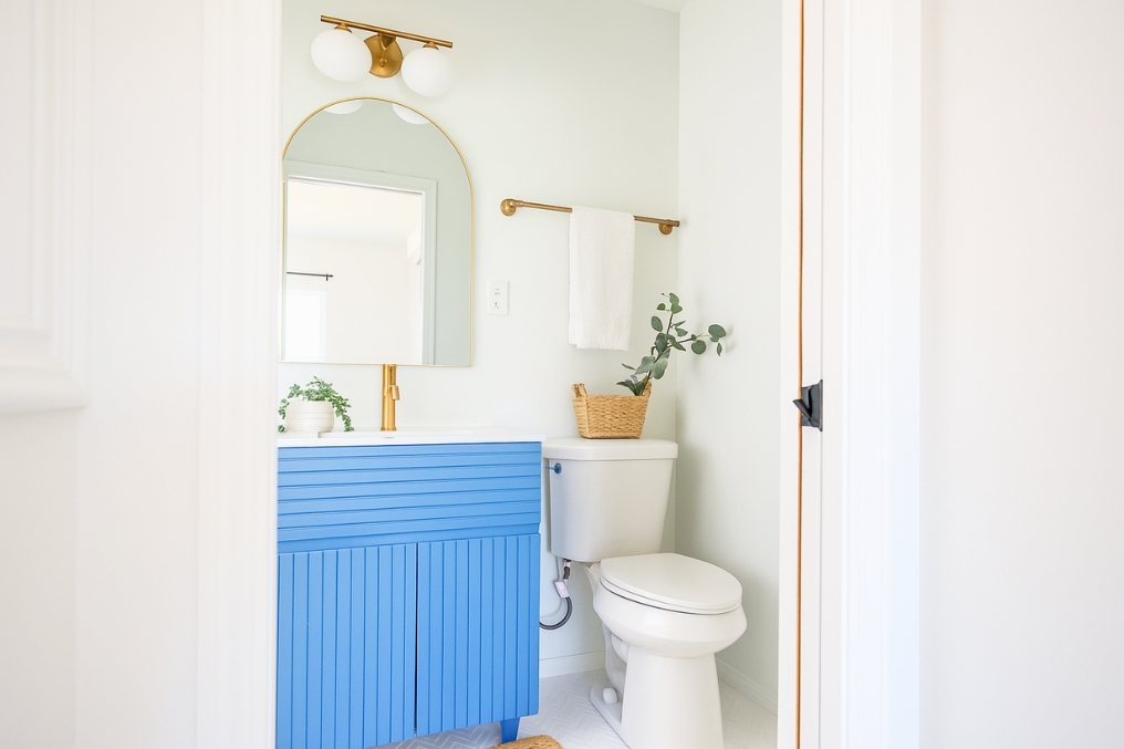 Bright and airy ADU bathroom with vibrant blue vanity, gold fixtures, and decorative accessories.